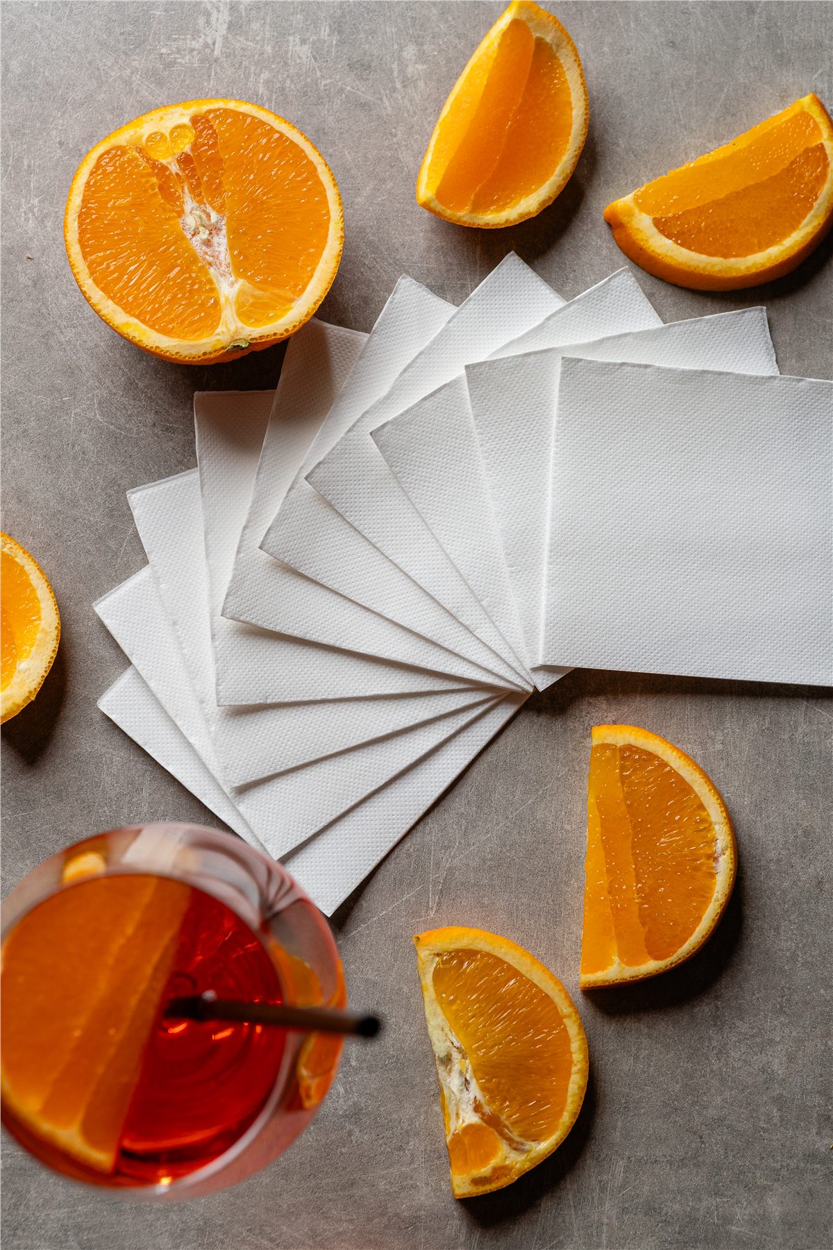 Fanned white napkins on stone with oranges and an Aperol spritz